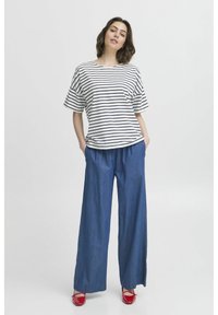 Bluză cu dungi, cu mânecă scurtă, albă și bleumarin, asortată cu pantaloni din denim cu talie înaltă și lejeri. Pantofi roșii. Siluetă simplă, relaxată.