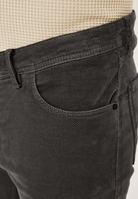 Dunkelgraue Cordhosen mit strukturierter Oberfläche, seitlichen Taschen und dezenten Nähten. Nahaufnahme des Taillen- und Taschenbereichs.