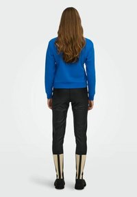 Felpa blu corta, pantaloni neri lucidi e stivali neri alti fino al ginocchio con righe verticali crema. Texture liscia e design aderente.