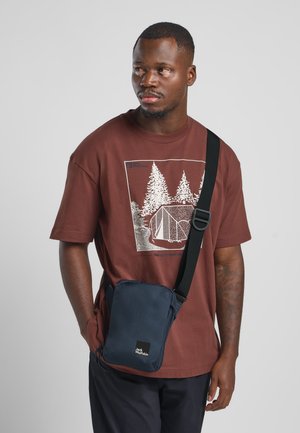 Borsa a tracolla blu navy con una cinghia nera regolabile, forma rettangolare, texture liscia, con una patch del logo sul davanti.