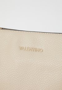 Borsa a tracolla in pelle beige con superficie testurizzata, caratterizzata da un logo dorato "Valentino" e impunture nere a contrasto lungo il bordo.