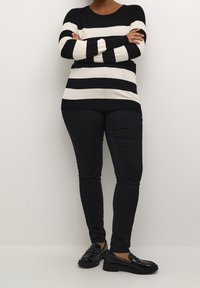 Haut à manches longues rayé noir et crème, associé à un jean skinny noir et des mocassins vernis noirs. Texture lisse, coupe décontractée et lignes épurées.