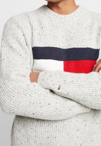 Hellgrauer, strukturierter Strickpullover mit horizontalen Farbblöcken in Marineblau, Weiß und Rot; mit gerippten Bündchen und einem kleinen Logo am Ärmel.