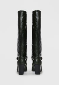 Bottes en cuir noir montantes avec une texture lisse, un talon carré et des fermetures éclaires sur les côtés, ornées d'une sangle et d'une boucle au niveau de la cheville.
