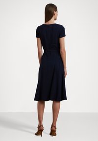 Abito blu navy con vita aderente e gonna a campana, maniche corte e zip sul retro. Il tessuto appare liscio con dettagli minimi.