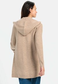 Beige Kapuzenstrickjacke mit geripptem Struktur, langen Ärmeln und lockerer Passform. Die Rückansicht zeigt die Nahtdetails und einen Saum, der über die Hüften reicht.