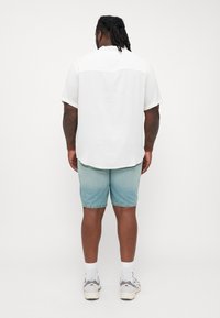 White short-sleeve shirt with back yoke, paired with light blue denim shorts, knee-length. Light-colored sneakers and white socks.