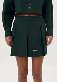 Donkergroene geplooide rok van zacht materiaal. Bevat een merklabel aan de zoom. De rok heeft een aansluitende tailleband voor een gepolijste look.