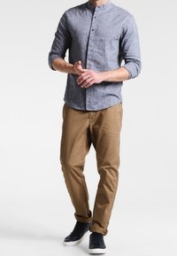 Camisa de botón gris claro con cuello mao, combinada con chinos beige y zapatillas oscuras. La camisa tiene mangas largas y una tela texturizada.