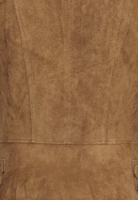 Bruine suède stof met een zachte textuur, voorzien van verticale naden en zijzakken, wat een gestructureerd maar eenvoudig ontwerp creëert.