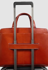 Borsa tote in pelle di un ricco arancione, con doppi manici e tracolla per il bagaglio, dalla texture liscia e design minimalista.