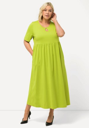 Abito maxi verde a maniche corte con colletto rotondo e dettaglio a chiave, caratterizzato da una vita arricciata e tasche laterali. Abbinato a tacchi neri.