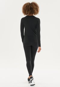 Schwarzes sportliches Longsleeve-Oberteil mit strukturierten Akzenten, kombiniert mit hoch taillierten schwarzen Leggings mit perforierten Details und Sportschuhen.