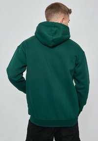 Sweatshirt à capuche verte en tissu doux, avec une coupe décontractée, des poignets et un ourlet côtelés, et une poche kangourou à l'avant.