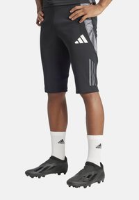 Zwarte sportshorts met een grijs paneel, voorzien van een logo met drie witte strepen, gecombineerd met witte sokken en zwarte voetbalschoenen met een gestructureerd ontwerp.