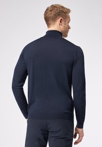 Dunkelblauer Strickpullover mit hohem Kragen, langen Ärmeln und gerippten Bündchen sowie Saum. Die glatte Textur und die taillierte Form heben das Design hervor.