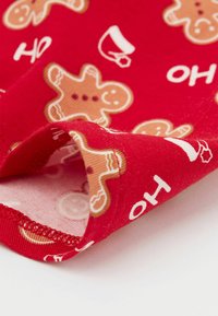 Červená látka s motivem perníčků a hrnků s bílými akcenty. Textura je hladká s mírným pružením.