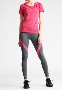 Urheiluasu, jossa on vaaleanpunainen hehkuva lyhythihainen paita ja harmaat legginsit vaaleanpunaisilla sivuaksenteilla sekä mustat kengät.