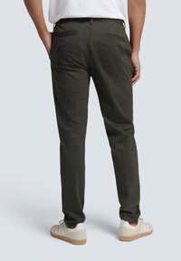 Dark green relaxed-fit trousers with a textured fabric, featuring two back pockets and a tapered design, paired with white sneakers.