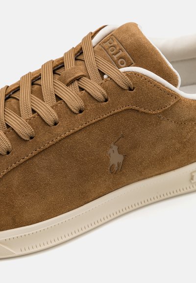 Tenis suede maro cu suprafață texturată, șireturi plate bej și interior alb. Prezintă un logo subtil pe lateral și o talpă plată din cauciuc.