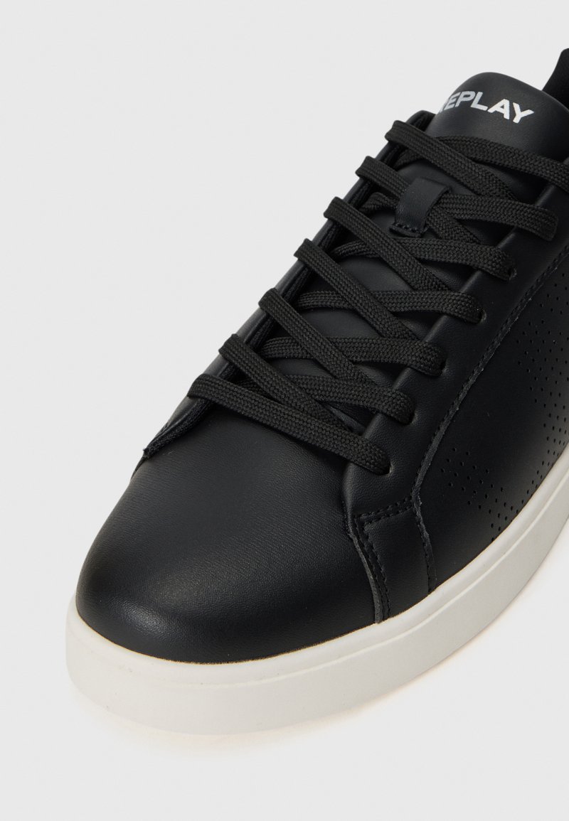 Zapatilla negra con cuero texturizado y suela blanca, con cordones planos negros y pequeñas perforaciones en el lateral, de la marca "REPLAY".