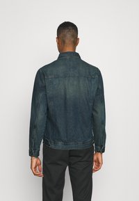 Jeansjacke, dunkelblau, klassischer Schnitt mit knöpfbaren Manschetten, Brustnähten und seitlichen Taschen. Glatte Textur mit einem leicht ausgewaschenen Finish.