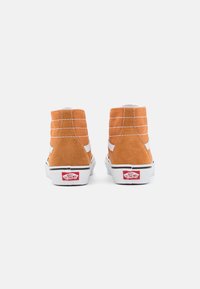 Zapatillas altas de ante naranja con rayas laterales blancas, paneles texturizados y acentos de talón en rojo y blanco con marca. La suela de goma es blanca.