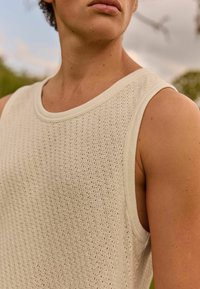 Lys beige strikket top med en struktureret mønster og brede ærmegab. Den glatte halsudskæring og det bløde stof forbedrer åndbarheden.