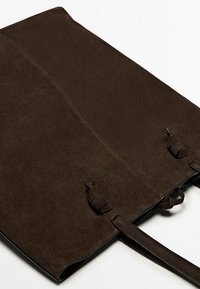 Sac messager en daim marron au design plat, avec deux sangles nouées et un bord en cuir noir lisse le long de l'ouverture. Aucun matériel visible ni motifs.