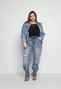 Jeansjakke, lys vask, slitte detaljer; svart blonde topp; avslappede jeans med hull; svarte høyhælte sandaler; rett silhuett.