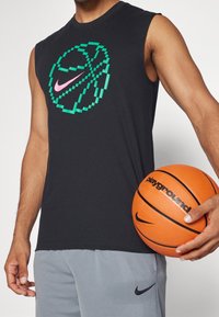 Débardeur noir avec un graphique de basket-ball pixelisé en vert et rose ; short de sport gris avec un petit logo Nike noir ; ballon de basket orange.