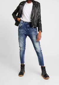 Svart läderbikerjacka, vit t-shirt och blå slitna jeans; kombinerat med svarta kängor med texturerad sula.