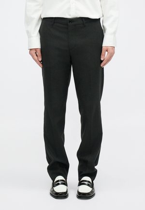 Crne krojene hlače ravnog kroja s patentnim zatvaračem i dugmetom, uparene s crno-bijelim lofericama i dugim bijelim košuljama.