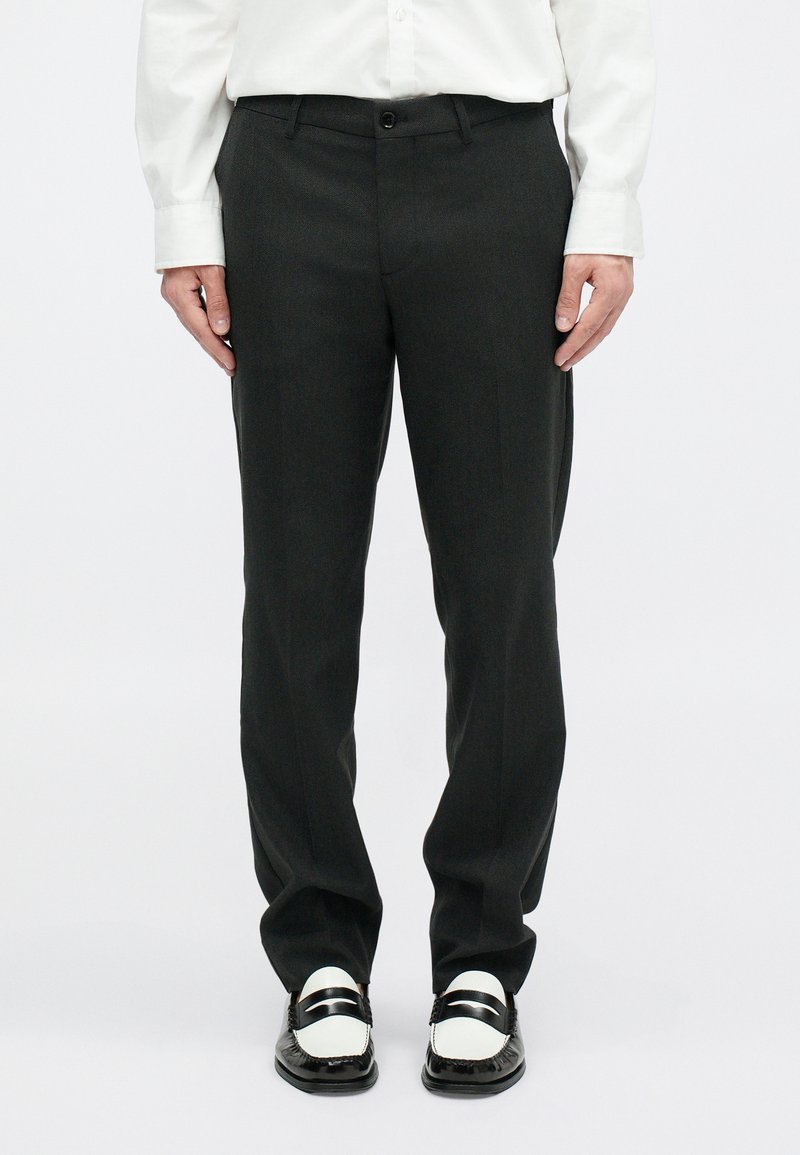 Czarne spodni na miarę o prostym kroju, z zapięciem na suwak i guzik, w połączeniu z czarno-białymi mokasynami i białą koszulą z długim rękawem.