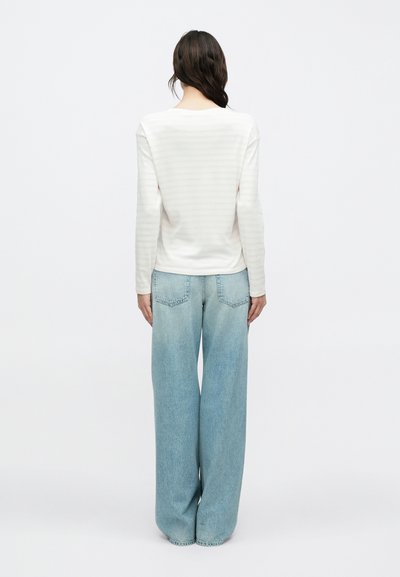 Λευκό τοπ με μακριά μανίκια και διακριτικές ρίγες, συνδυασμένο με ανοιχτό μπλε τζιν παντελόνι φαρδιάς γραμμής. Μείγμα βαμβακιού, άνετη εφαρμογή, απαλή υφή.