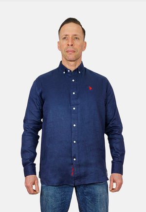 Camicia azzurra navy in tessuto leggero, con un piccolo logo rosso, bottoni bianchi e uno spacco laterale con dettagli di cucitura rossa.