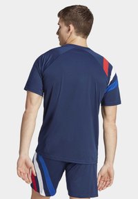 Marineblauw sportshirt met korte mouwen, voorzien van kleurgeblokte accenten in rood, wit en blauw op de schouder. Gladde, lichte stof.