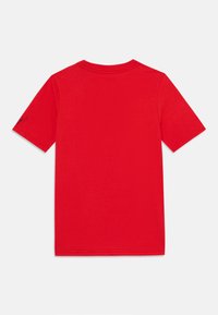 Camiseta de algodón roja con mangas cortas, cuello redondo, diseño liso y un pequeño detalle gráfico negro en la manga izquierda.