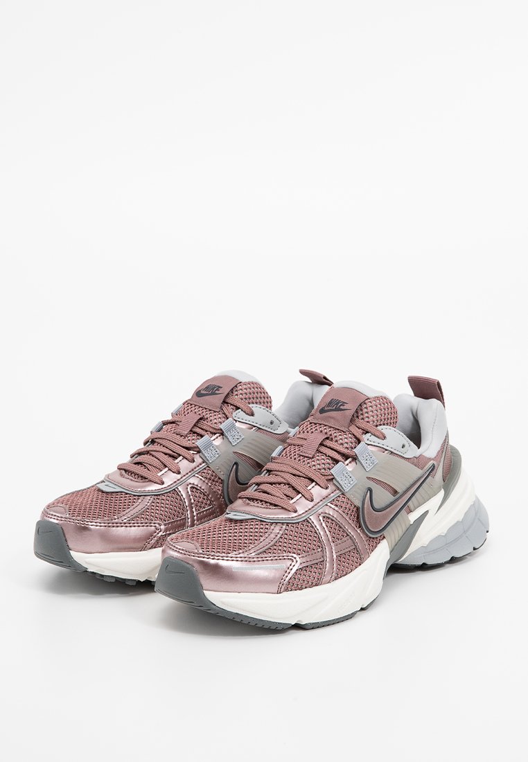 Zapatos deportivos Nike con parte superior de malla en oro rosa, detalles en gris y una suela blanca gruesa. Presenta un cierre de cordones en la parte delantera y un detalle del logo.