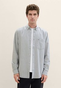 Randig knappskjorta i ljusblått och vitt, tillverkad av bomull. Har en påsficka, knappmanschetter och en krage. Bärs över en vit t-shirt.