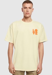 Cremefarvet bomulds T-shirt med korte ærmer, prydet med en orange "LOVE" grafisk design på venstre brystområde.