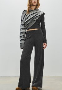 Pantaloni grigi a gamba larga abbinati a un top nero aderente a maniche lunghe, completati da uno scialle a righe grigio e blu navy in maglia. Tessuto strutturato.