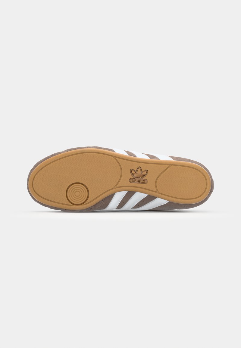Sportschuhsohle mit einer braunen Gummibasis, weißen Streifen und einer strukturierten Oberfläche. Verfügt über ein kreisförmiges Designelement in der Nähe der Ferse.