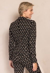 Schwarz-beiger Blazer mit Muster, langen Ärmeln, tailliertem Schnitt, strukturierten Schultern und strukturierter Stoff. Rückansicht gezeigt.