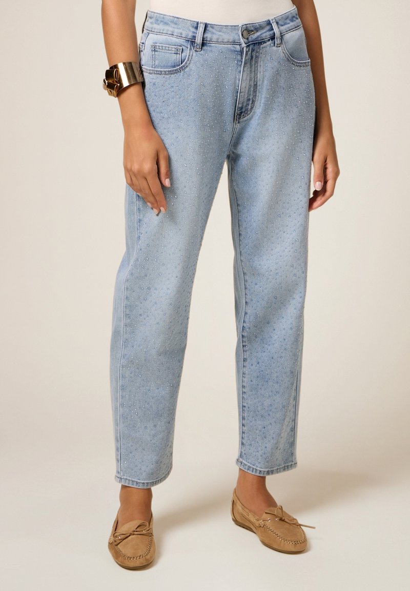 Jeans de denim azul claro con un corte relajado, que presentan un sutil acabado texturizado, cinco bolsillos y una cintura de altura media. Combinados con mocasines beige.