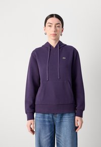 Violetinė pavadinimo sukapota džemperis, pagamintas iš medvilnės, su priekiu kišene, raišteliu ir maža žalia logotipu krūtinėje. Laisvas, su elasticinėmis rankovėmis.