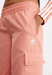 Vaahtokarkkipinkit cargo-housut, joissa on joustava vyötärö, sivutasku ja valkoinen Adidas-logo. Sileä pinta, rento istuvuus ja muotoiltu malli.