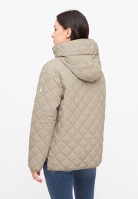 Beige gewatteerde jas met een capuchon, voorzien van een diagonaal patroon, zijzakken en een logo op de linker mouw. Gladde textuur en een casual ontwerp.