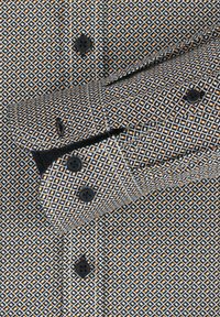 Patterned shirt in black, white, and orange with diamond shapes, featuring black buttons and contrasting cuff design. Cotton blend texture visible.