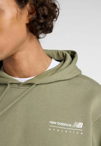 Olijfgroene hoodie van een katoenmix, met een capuchon met trekkoord en witte logo tekst "new balance ATHLETICS" op de borst.